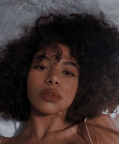 a woman with curly hair laying down on a white furnishing area and looking at the camera