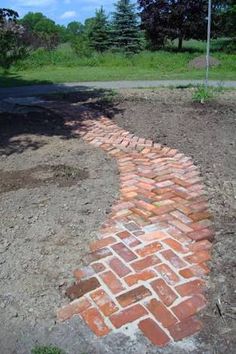 a brick path is shown in the middle of a dirt area with grass and trees behind it