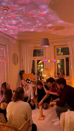 a group of people sitting on the floor in a living room with colorful lights above them