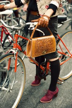 a woman is standing next to her bike with a purse on the handlebars