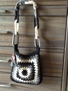 a crocheted purse hanging on a wooden wall with drawers in the back ground