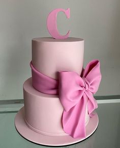 a pink cake with a large bow on the top and letter c on the side