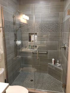 an image of a bathroom with grey tile on the walls and shower stall door open