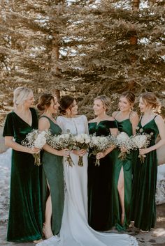 a group of women standing next to each other in front of snow covered trees and holding bouquets