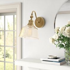 a vase with flowers sitting on top of a table next to a wall mounted light