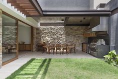 an outdoor kitchen and dining area with grass on the ground, surrounded by stone walls