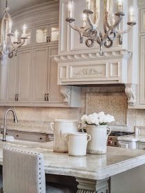 a chandelier hangs over a kitchen island with two cups on it and flowers in the middle