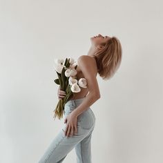 a woman holding flowers in her right hand and looking up at the sky with one eye closed