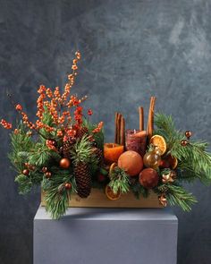 an arrangement of fruit, candles and pine cones is displayed on a gray box with evergreen branches