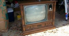 an old tv sitting on top of a wooden stand next to a pile of boxes