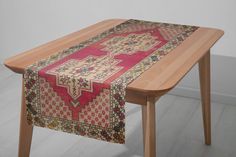 a wooden table with a red and yellow rug on it's top, sitting in front of a white wall