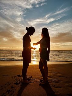 two people are standing on the beach at sunset, facing each other and shaking hands