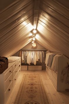 an attic bedroom with white furniture and clothes hanging on the rack in front of it