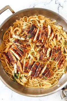 a pan filled with chicken and pasta on top of a white marble countertop next to utensils