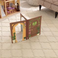 an open cardboard doll house on the floor in a living room with furniture and accessories