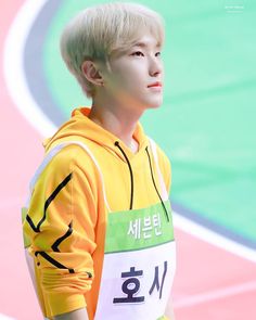 a young man with blonde hair wearing a yellow hoodie and standing on a track