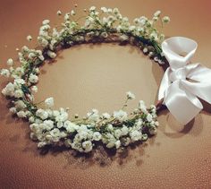 a white flowered wreath with a bow on the side sitting on a brown surface