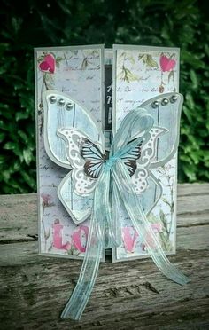 a card with a butterfly on it sitting on top of a piece of wood in front of some bushes