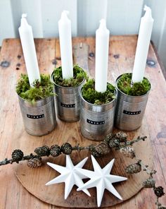 a wooden table topped with four metal buckets filled with moss and white candle holders