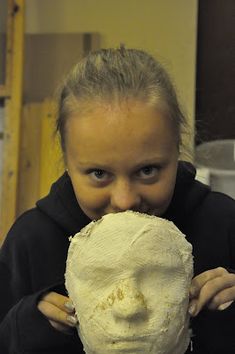 a woman is holding up a white mask to her face and looking at the camera