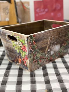 a wooden box sitting on top of a checkered tablecloth covered table with deer and berries painted on it