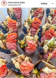 an assortment of meats and cheeses on skewers with fruit in bowls