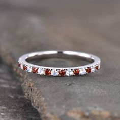 a white gold band with red and white stones on it, sitting on top of a rock