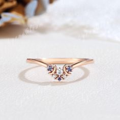 a gold ring with two diamonds on it sitting on a white surface next to a flower