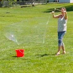 a woman is playing with a sprinkler in the grass near a red bucket