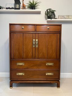 a large wooden dresser with brass handles and drawers on the top, against a white wall