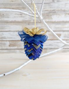 a pine cone ornament hanging from a twig on a branch with ribbon