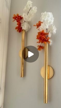 two gold vases with white and orange flowers in them are on the wall next to each other