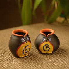 two black and orange vases with faces painted on them sitting on a brown surface