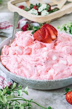 a bowl full of strawberry fluff with two strawberries on the side and another bowl in the background