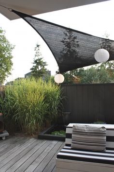 an outdoor area with wooden decking and black awnings over the seating area