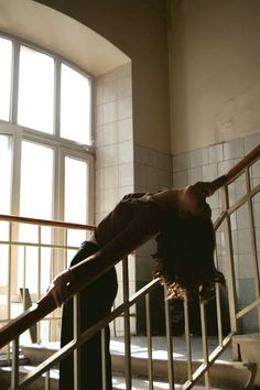 a woman leaning on the handrail of a stair case in front of a window