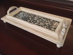 a white tray sitting on top of a wooden table next to a mirror with an ornate design