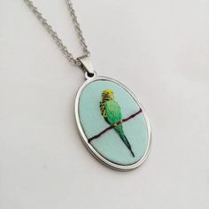 a green bird sitting on top of a tree branch in a glass dome pendant necklace