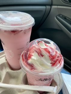 two drinks in plastic cups with strawberries and whipped cream