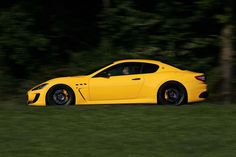 a yellow sports car driving on the road at night time with trees in the background