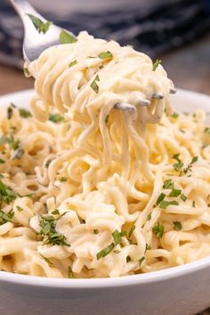 a white bowl filled with noodles and parsley on top of a wooden table next to a blue pot