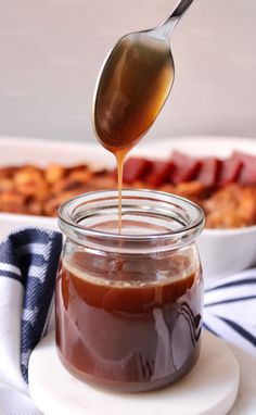 a spoon full of caramel sauce being drizzled into a glass jar