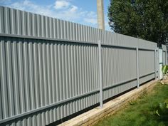 a large gray metal fence next to a lush green field