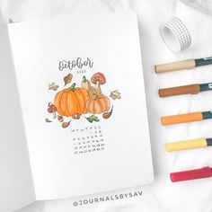 an open notebook with markers and pencils next to it on a white sheet that says october