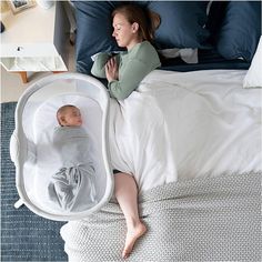 a woman laying on top of a bed next to a baby in a crib