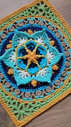 a crocheted square with a flower in the center on a wooden surface,