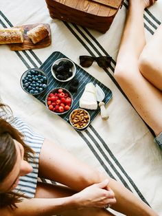 a woman is sitting on the bed with her legs crossed while eating fruit and cheese