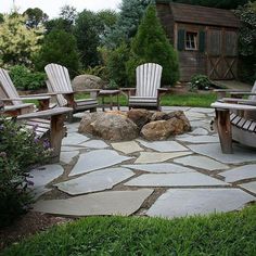 a stone patio with wooden chairs and rocks in the middle, surrounded by greenery