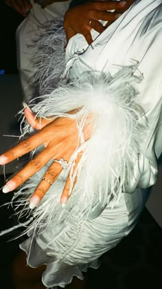 a woman with her hands on the arm of another person wearing white feathered dress