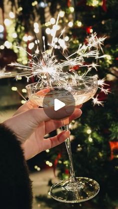 a person holding a wine glass in front of a christmas tree with sparklers on it